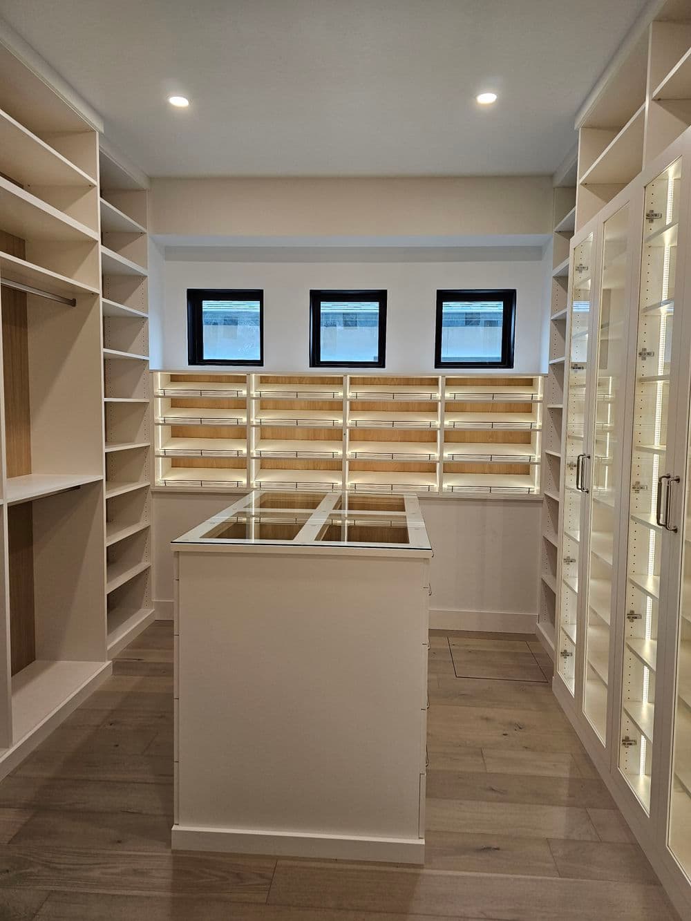Spacious modern walk-in closet with shelving and glass display cabinets illuminated by LED lights.