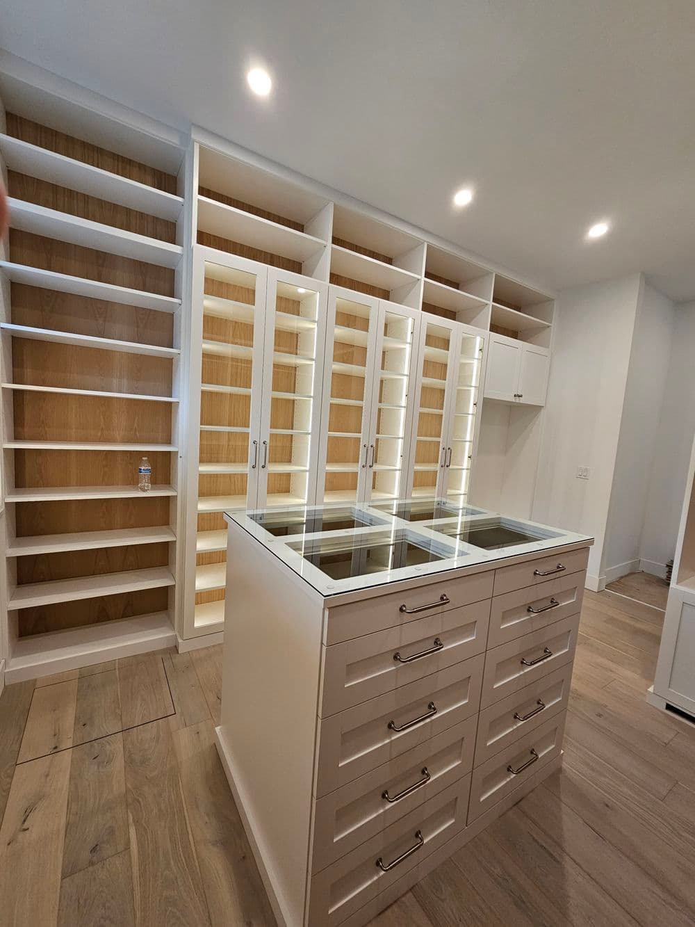 Elegant white walk-in closet with glass-top island and ample shelving. Modern storage solution.