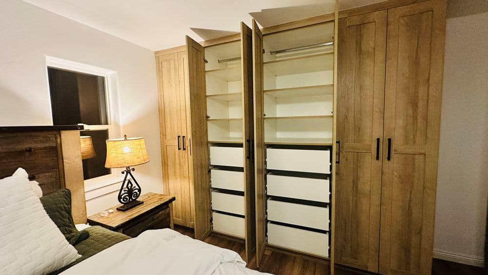 Modern bedroom with open wooden wardrobes and a bedside lamp, showcasing storage options.