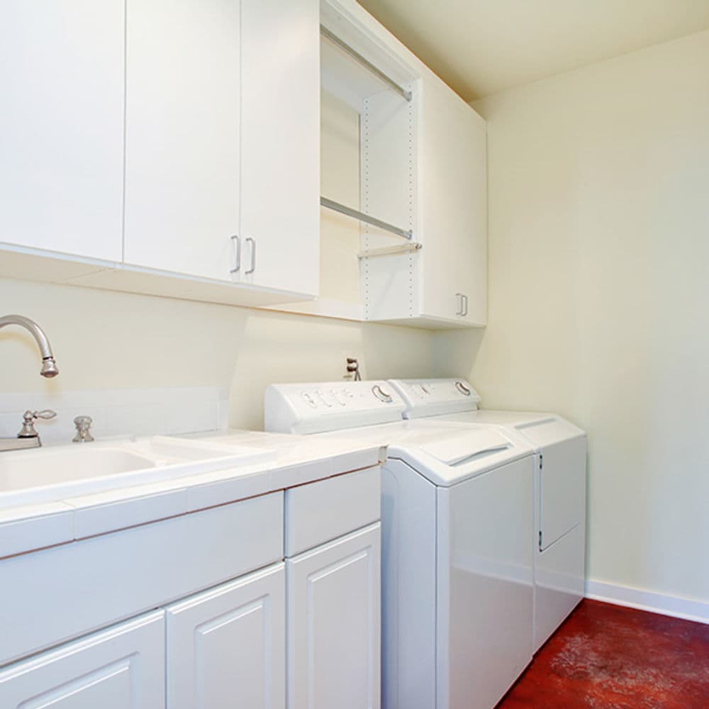 Bright laundry room with white cabinets, sink, and modern washer-dryer set.