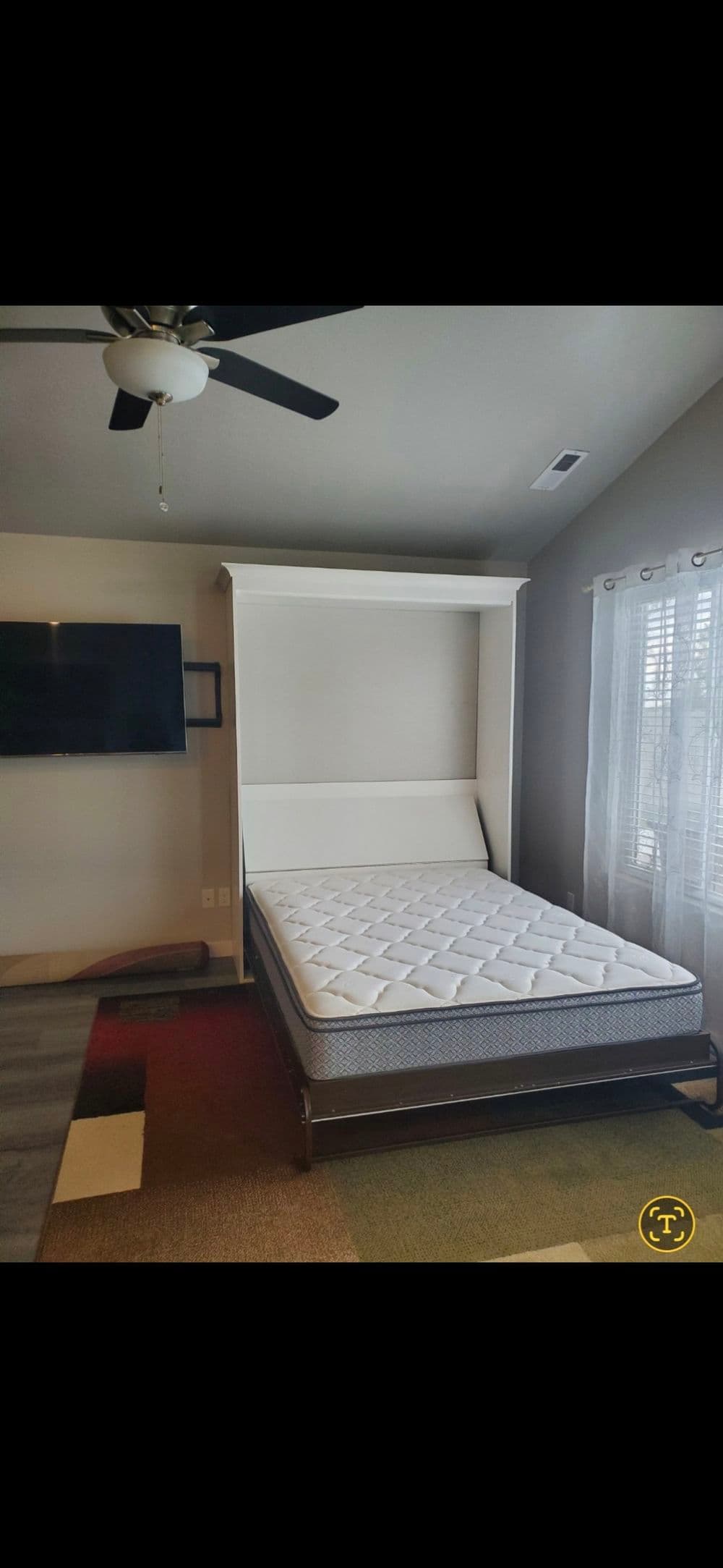 Murphy bed in modern room with mattress extended and wall-mounted TV in background.