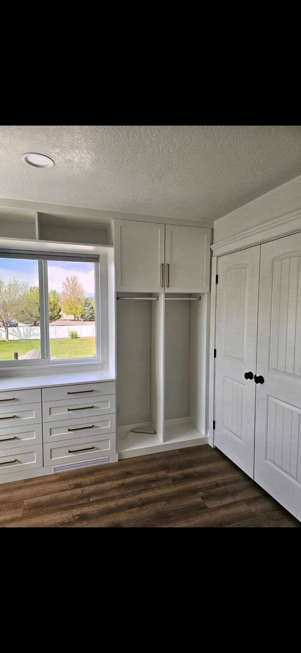 Modern bedroom with white storage cabinets, drawers, and a large window showcasing outdoor view.