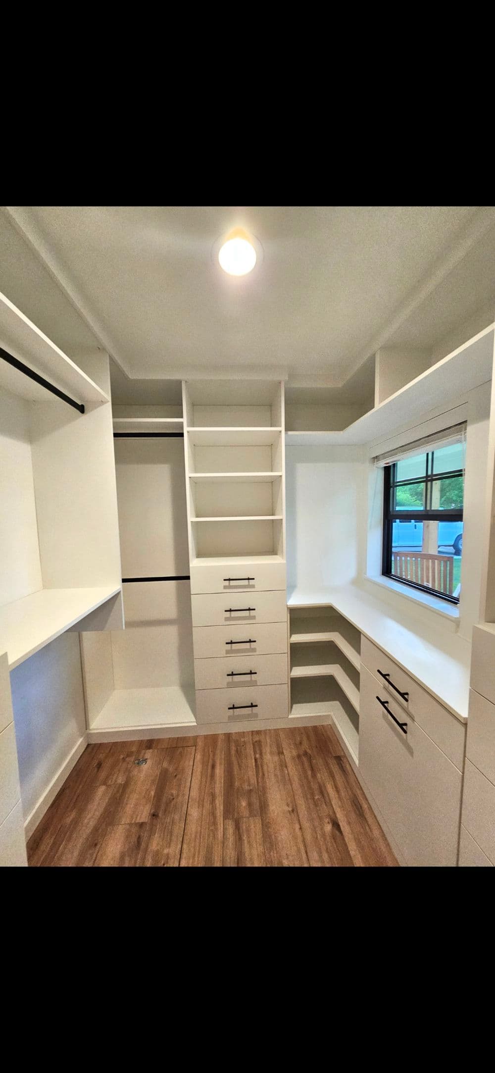 Spacious modern closet with white cabinetry, shelves, and wood flooring. Natural light from window.