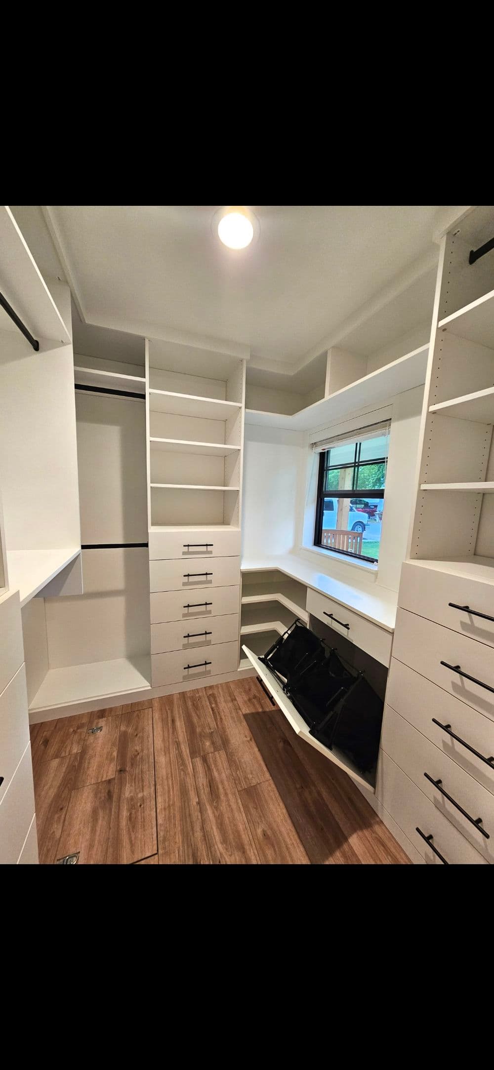 Modern walk-in closet with custom shelving, drawers, and large window, featuring wood flooring.