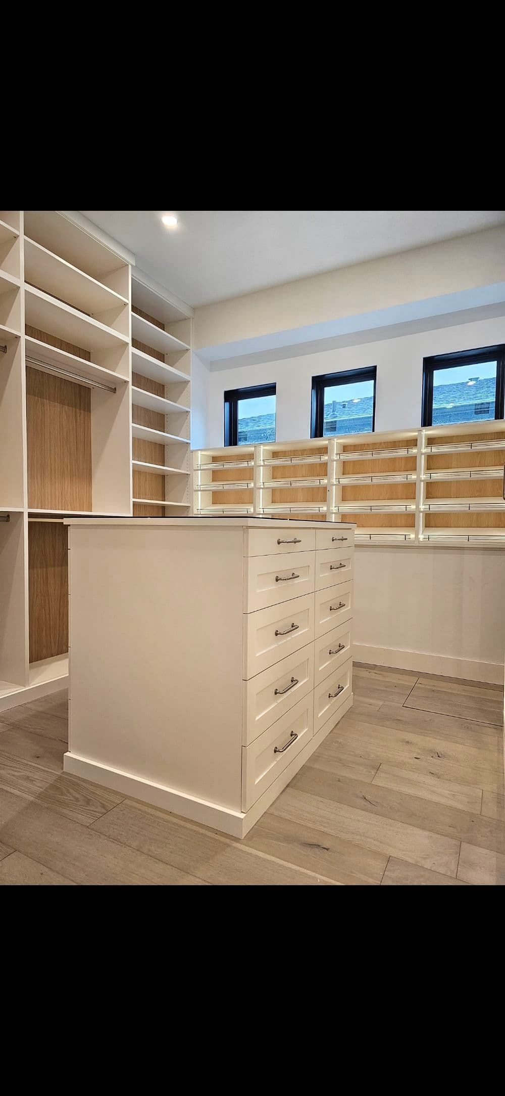 Stylish modern walk-in closet with white cabinetry, spacious drawers, and wooden shelves.