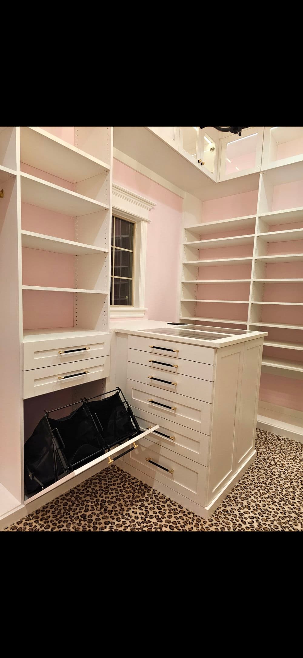 Elegant walk-in closet with white cabinetry, pink walls, and leopard print carpet.