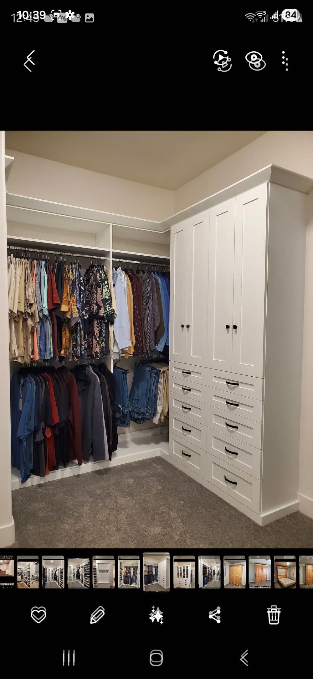 Modern walk-in closet with organized clothing racks and white cabinetry housing drawers.