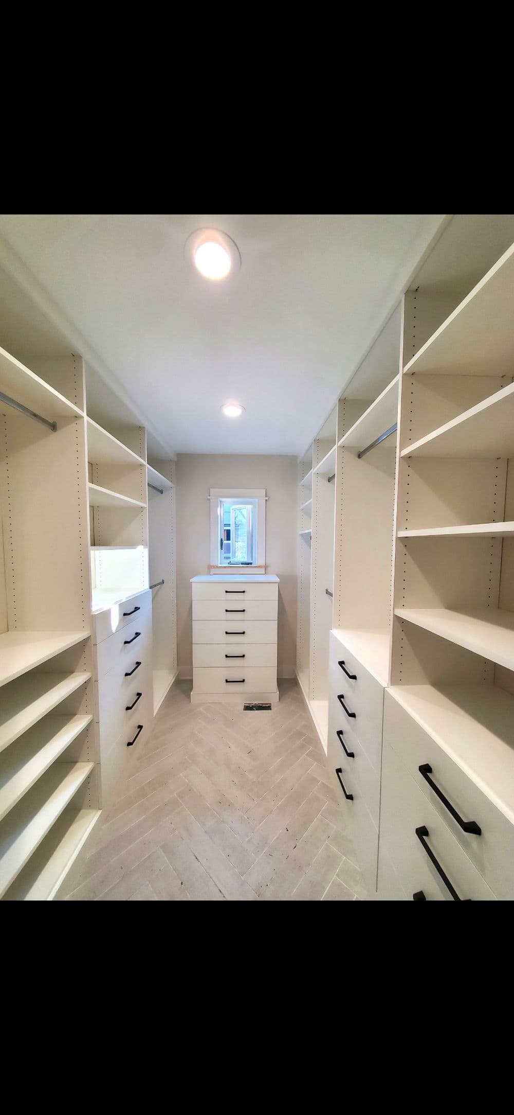 Spacious walk-in closet with modern shelves and herringbone floor design.
