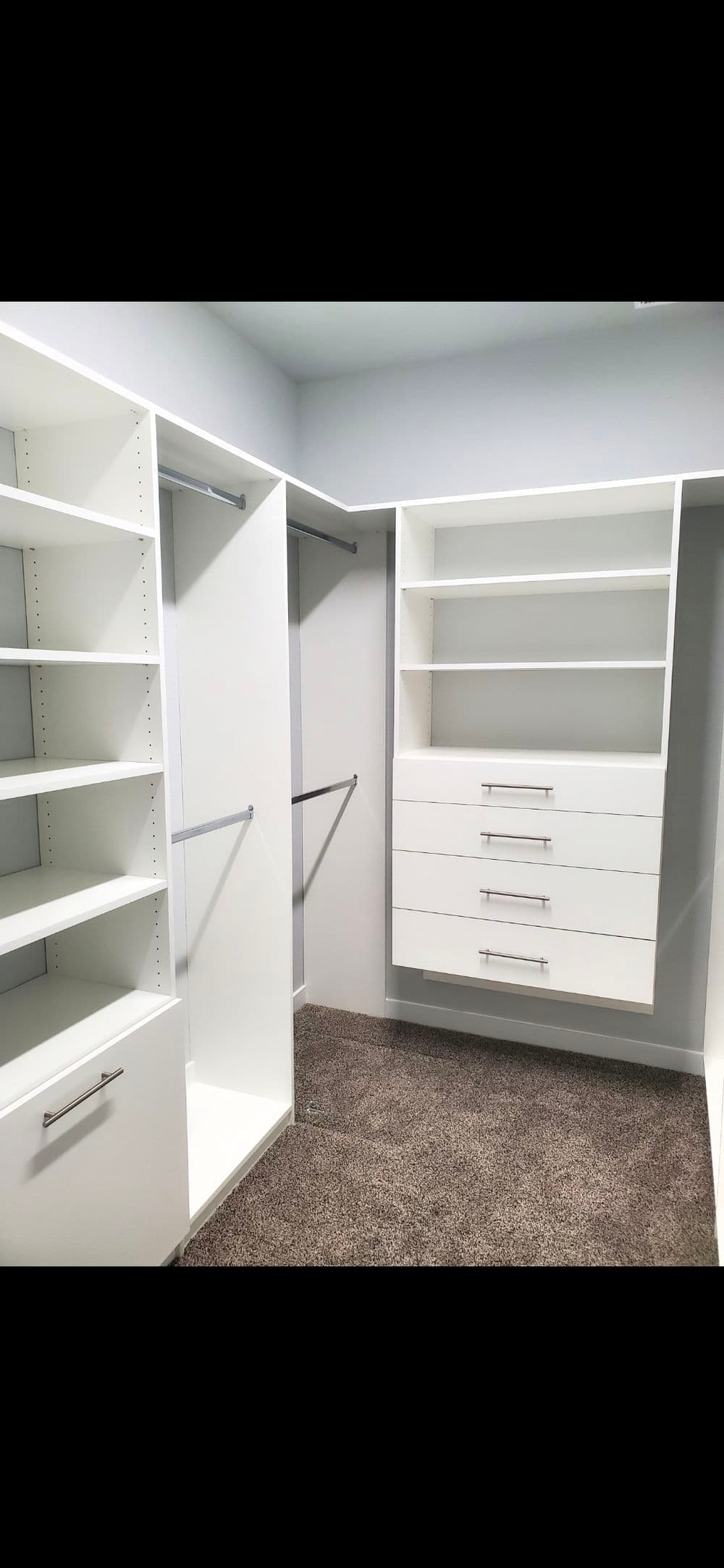 Modern white walk-in closet design with shelves and drawers on carpeted floor.