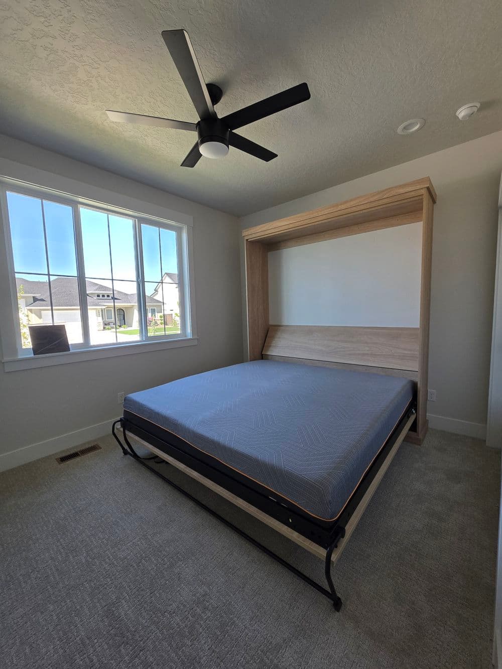 Modern bedroom with a fold-down bed, ceiling fan, and large windows letting in natural light.
